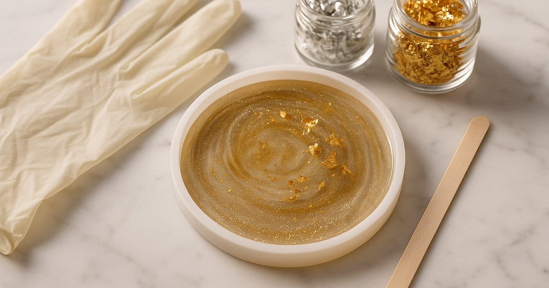 Round silicone resin mold with gold glitter and metallic flakes surrounded by resin craft supplies on marble surface