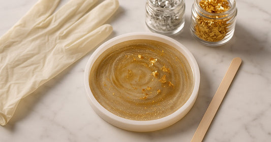 Round silicone resin mold with gold glitter and metallic flakes surrounded by resin craft supplies on marble surface