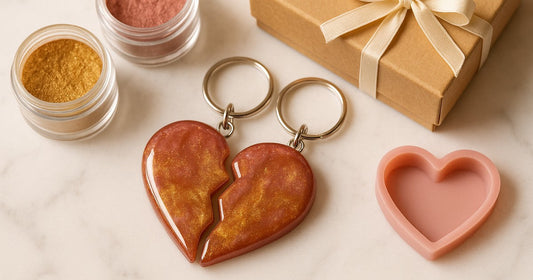 Two matching resin broken heart keychain halves in dusty rose and gold mica finish placed on white marble with craft materials