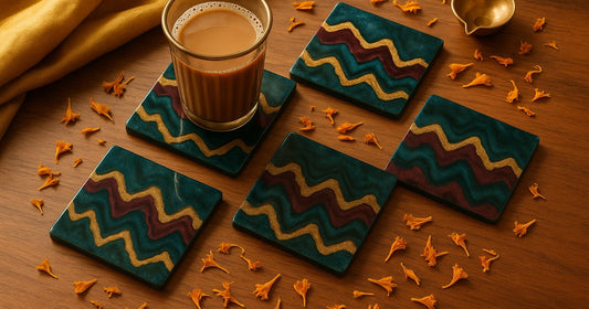 Handmade square zigzag resin coaster set in teal, burgundy, and gold on a teak wood surface with chai glass and Indian festive décor