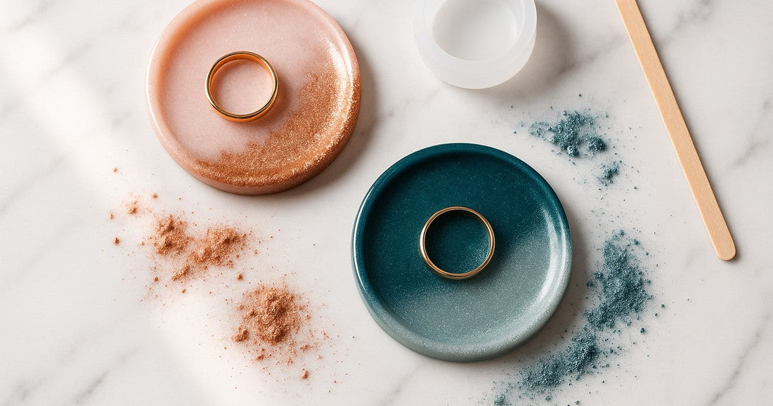 Handmade resin ring holder dishes with mica gradient finish in blush pink and teal, with gold rings resting inside, on a white marble surface