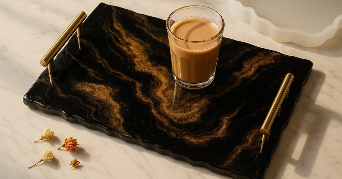 Handmade resin serving tray with black and gold mica swirl design, gold handles, on a marble surface